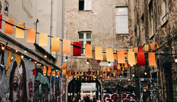 Striscioni di carta colorati e lucine pendono lungo uno stretto vicolo urbano, decorato con graffiti su muri di edifici rovinati.