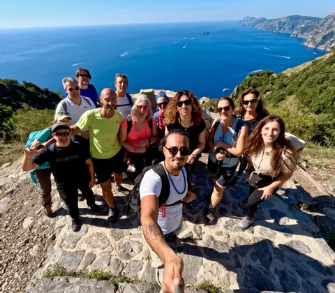 Eine WeRoad-Wandergruppe macht ein Selfie auf einer sonnigen Klippe mit Blick auf das blaue Meer und die Küste.