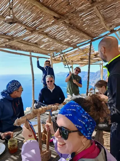 Eine WeRoad-Gruppe versammelt sich an einem Holztisch unter einem Reetdach, mit Blick auf das Meer und die Küstengebirge.