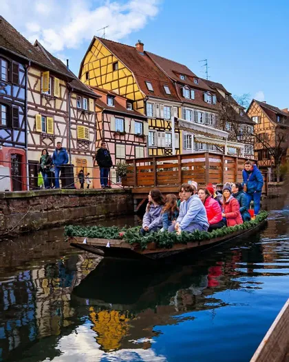 Un viaje en grupo de WeRoad hace un recorrido en barco por un canal, con coloridos edificios de entramado de madera reflejados en el agua.