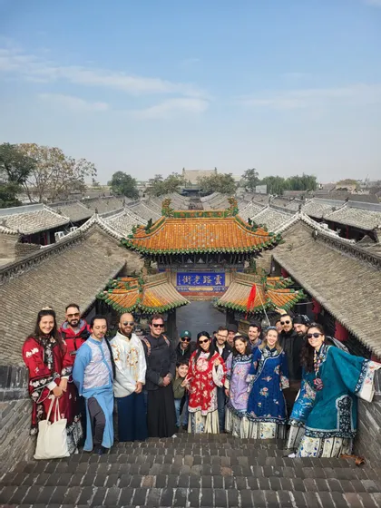 Un viaggio di gruppo WeRoad posa su gradini di pietra in costumi tradizionali asiatici, con i tetti di una città storica sullo sfondo.