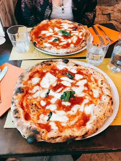 Two Neapolitan pizzas topped with fresh mozzarella and basil resting on a restaurant table with glasses of water.