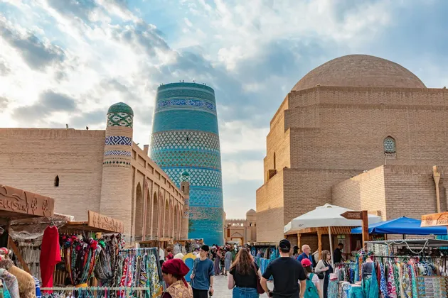 Eine WeRoad-Gruppenreise erkundet einen geschäftigen Freiluftmarkt mit einem großen, blau gekachelten Minarett und alten Backsteingebäuden im Hintergrund.
