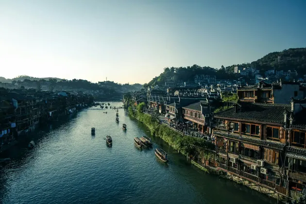 Una vista dall'alto di piccole barche su un fiume che attraversa un borgo tradizionale con edifici lungo le rive.