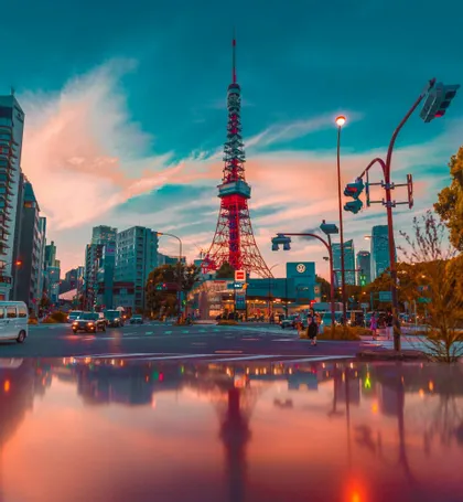 La Torre di Tokyo rossa si erge su un paesaggio urbano al tramonto, il suo riflesso visibile su una strada bagnata in primo piano.