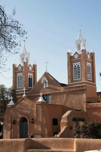 Una chiesa in stile adobe con due campanili gemelli dalla cima bianca si staglia contro un cielo azzurro e limpido.