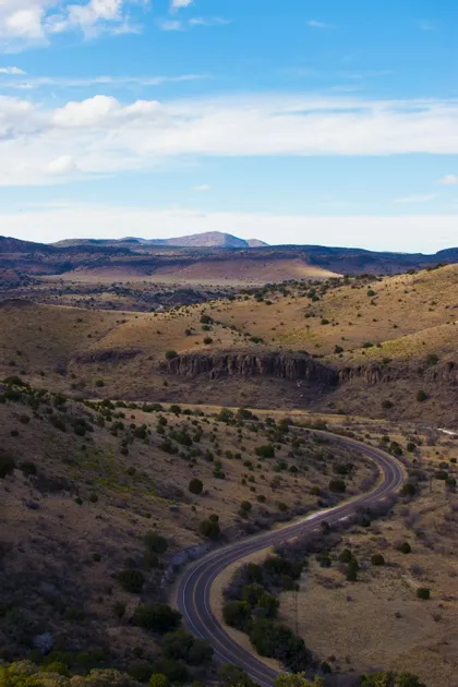 Una strada asfaltata che serpeggia tra colline aride e ondulate, punteggiate da arbusti verdi, ripresa da un punto panoramico elevato.