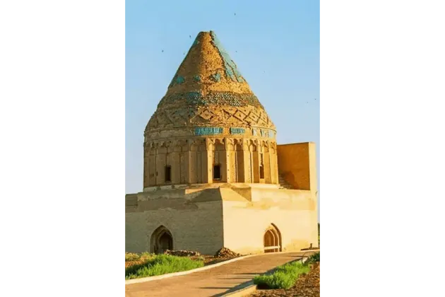 Mausoleo storico in pietra color sabbia con cupola conica, dettagli in piastrelle blu e intricato lavoro in mattoni.