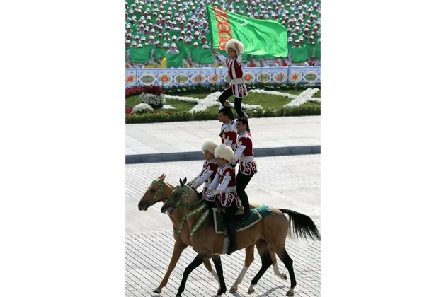Un bambino sventola la bandiera del Turkmenistan dalla cima di una piramide umana formata da artisti equestri in abiti tradizionali.