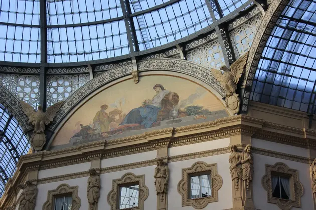 El interior ornamentado de una galería, con un gran mural, intrincadas esculturas y un alto techo de cristal abovedado.
