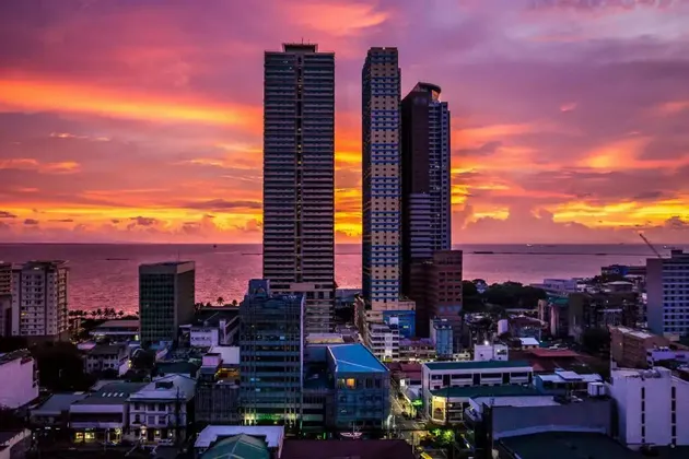 Una veduta aerea dei grattacieli di una città costiera, con un vivace tramonto arancione e viola sull'oceano.