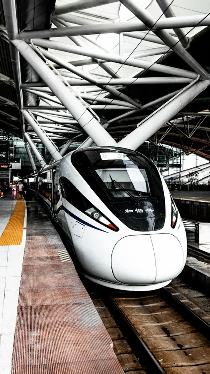 Un treno bianco ad alta velocità si è fermato sulla banchina di una stazione sotto un moderno tetto metallico geometrico.