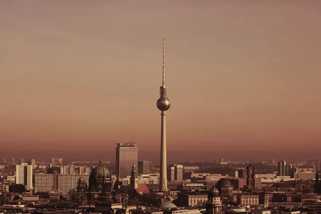 Una alta torre de televisión con una plataforma de observación esférica se eleva sobre un denso horizonte urbano bajo un cielo brumoso y de tonos cálidos.