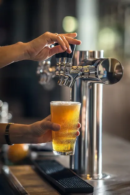 Primer plano de manos sirviendo una cerveza dorada de un grifo cromado brillante en un vaso de pinta.