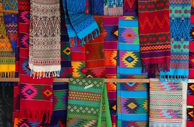 Una collezione di tessuti colorati intrecciati con intricati motivi geometrici e bordi frangiati esposti.
