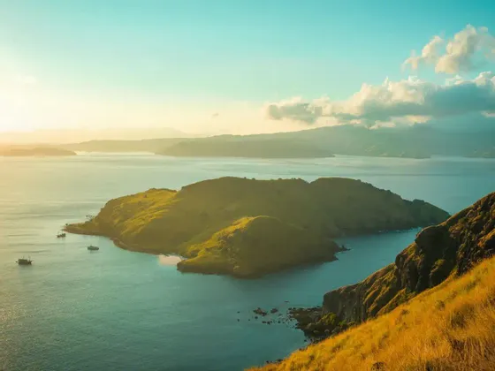Il sole dorato illumina verdi isole che si susseguono in un mare blu sereno, viste da una collina costiera erbosa.