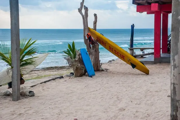Una tavola da surf gialla per il salvataggio e altre tavole da surf sono appoggiate su una spiaggia sabbiosa con l'oceano sullo sfondo.