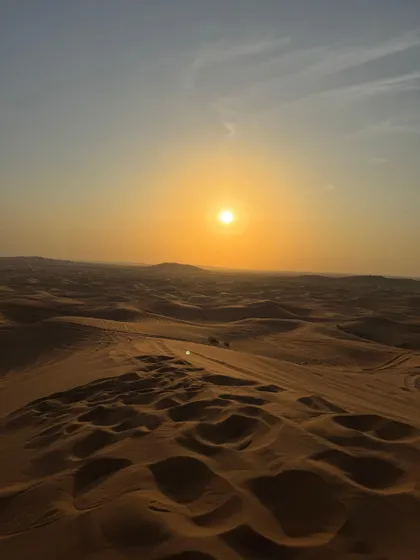 Il sole al tramonto proietta un bagliore dorato su una vasta distesa di sinuose dune di sabbia desertiche sotto un cielo velato.