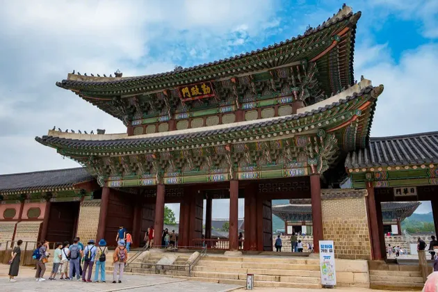 Un gruppo di turisti si trova in un cortile di fronte a un grande portale tradizionale asiatico con un tetto a pagoda finemente dipinto.