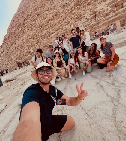 Ein Mann macht ein Selfie mit einer WeRoad-Gruppe, die gemeinsam am Fuße einer großen Steinpyramide posiert.
