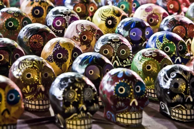 Una collezione di teschi calavera colorati e dipinti a mano, decorati con motivi intricati e glitter, esposti insieme.