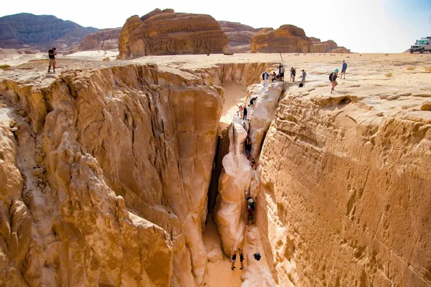 A WeRoad group trip of people climbing through a narrow sandstone canyon in a vast desert landscape.