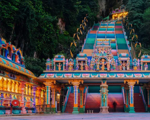 La scalinata colorata e illuminata di un sontuoso complesso templare, incastonata nel fianco di una ripida scogliera verde.