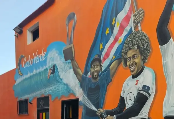 Un murale colorato su un edificio arancione celebra i surfisti di Capo Verde, raffigurandoli con un trofeo, una bandiera e champagne.