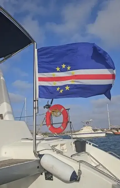 La bandiera di Capo Verde sventola su un'asta a poppa di una barca, con un salvagente visibile sotto in un porto.