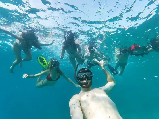Eine WeRoad Gruppenreise macht beim gemeinsamen Schnorcheln im klaren blauen Wasser ein Unterwasser-Selfie.