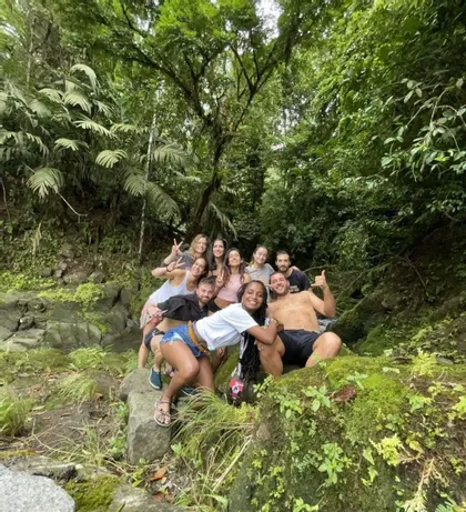 Eine WeRoad-Gruppe lächelt und posiert für ein Foto auf moosbewachsenen Felsen in einem dichten grünen Dschungel.