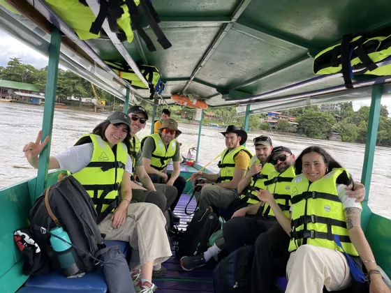 Gruppo WeRoad sorridente in barca sul fiume con giubbotti di salvataggio gialli.