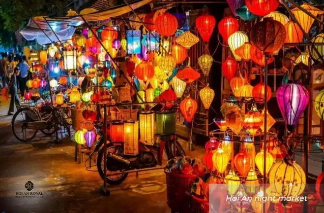 Una bancarella del mercato notturno piena di dozzine di lanterne colorate e luminose di varie forme, con una bicicletta parcheggiata davanti.