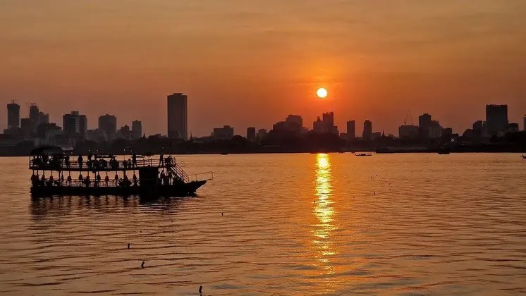 Un viaggio di gruppo WeRoad su un battello a due piani naviga sull'acqua al tramonto, con lo skyline di una città in silhouette sullo sfondo.