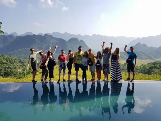 Un gruppo WeRoad in viaggio posa al bordo di una piscina a sfioro, con i riflessi nell'acqua e un paesaggio montuoso sullo sfondo.