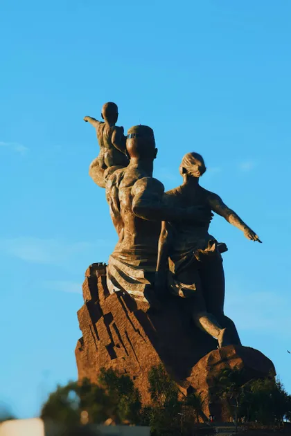 Un gran monumento de bronce de una familia, un hombre, una mujer y un niño, de pie sobre un pedestal rocoso contra un cielo azul claro.