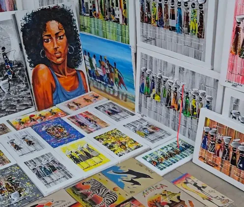 Eine Sammlung farbenfroher Leinwandbilder, darunter ein Frauenporträt, die afrikanische Motive zeigen und an einem Marktstand präsentiert werden.