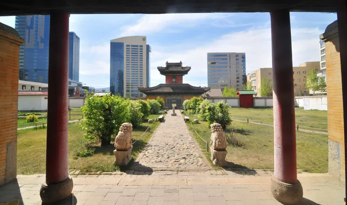Un temple traditionnel dans une cour verdoyante est encadré par des piliers rouges, avec des gratte-ciel modernes s'élevant en arrière-plan.