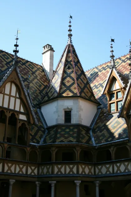 Un tetto in tegole smaltate di un edificio storico con motivi geometrici, visto da un cortile interno sotto un cielo azzurro.