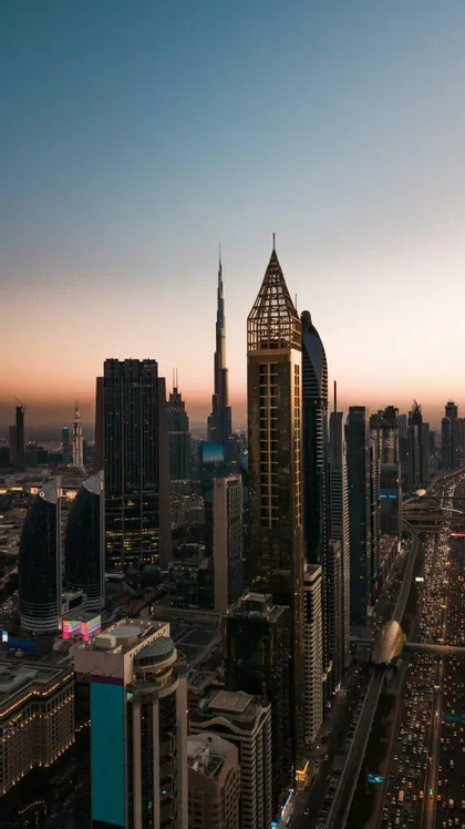 Una vista panoramica di un moderno skyline cittadino con grattacieli al tramonto, e sotto autostrade trafficate e una linea della metropolitana.