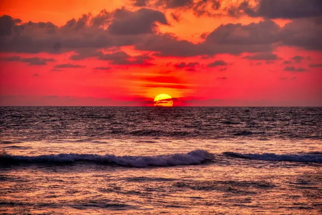 Le soleil se couche sur l'océan, projetant une lueur vibrante rouge et orange sur l'eau et un ciel nuageux.