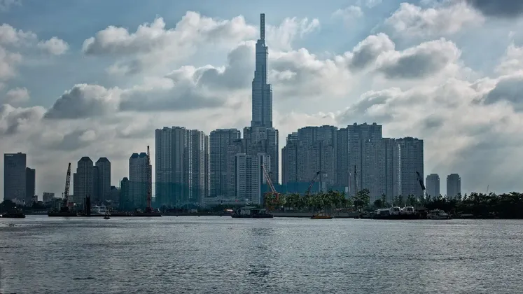 Uno skyline moderno con un grattacielo imponente, visto da oltre uno specchio d'acqua sotto un cielo parzialmente nuvoloso.