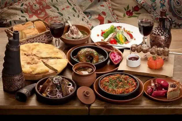 Eine reichhaltige Auswahl traditioneller Speisen, darunter Eintöpfe, Fladenbrot, Salate und gegrilltes Fleisch, serviert mit Rotwein auf einem Holztisch.