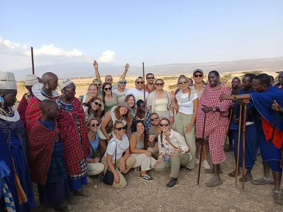 Eine WeRoad Gruppenreise posiert für ein Gruppenfoto mit Massai in traditioneller Kleidung in einer Savanne.