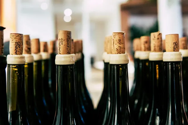 Un primo piano di bottiglie di vino verde scuro in fila, con focus sui tappi marchiati inseriti nei colli delle bottiglie.