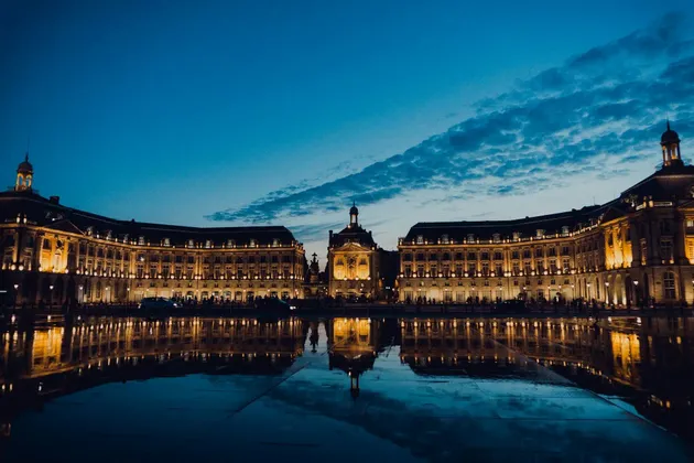 Un edificio storico illuminato che si riflette in un ampio specchio d'acqua al tramonto sotto un cielo blu intenso.