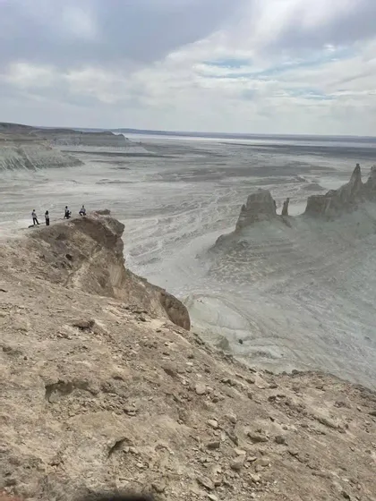 Un gruppo WeRoad di quattro persone in piedi sul bordo di una scogliera rocciosa, affacciato su un vasto canyon arido con guglie di roccia sotto un cielo nuvoloso.