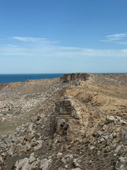 Una costa frastagliata e rocciosa, con scogliere a picco e vegetazione rada, si affaccia su un mare blu e tranquillo sotto un cielo sereno.
