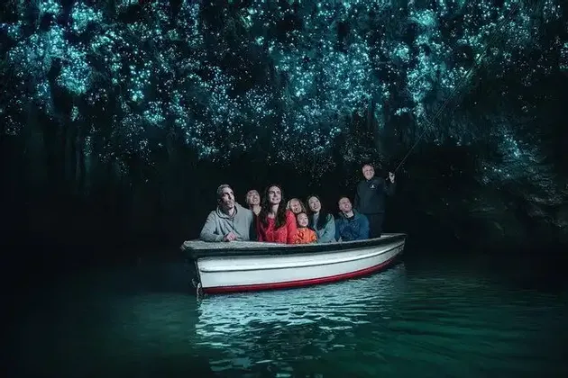 Eine WeRoad-Gruppenreise im Boot bestaunt die biolumineszenten Glühwürmchen an der Decke einer dunklen Höhle.