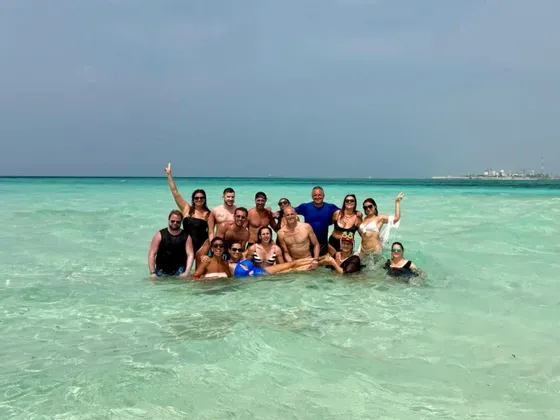 Un groupe WeRoad prend la pose pour une photo, debout dans l'eau claire et turquoise de l'océan, sous un ciel gris.